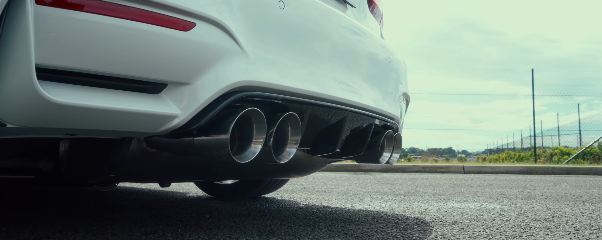 White BMW F80 M3 sports car with quad xForce exhaust tips on road.